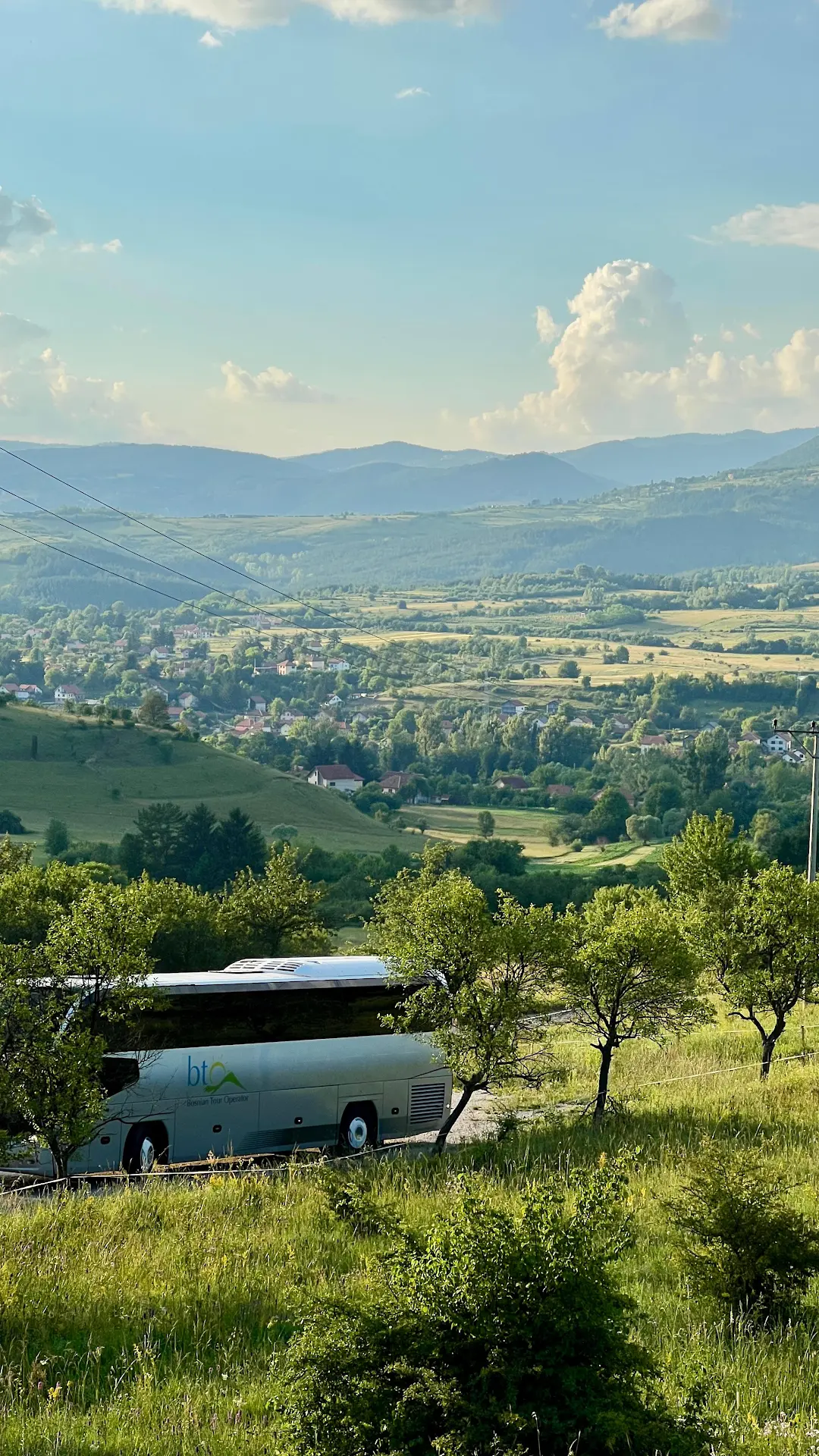 Just Tour coach parked above a green Bosnian valley of rolling hills, villages and distant mountains