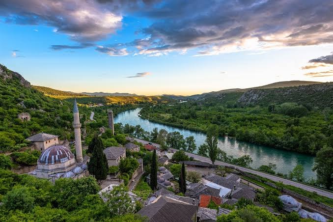 Sunset panorama of Počitelj in Bosnia and Herzegovina, with the Hadži Alija Mosque and minaret above village rooftops and the emerald Neretva River
